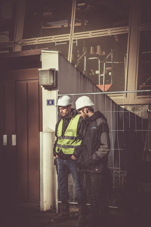 Two construction workers in hard hats discussing an incident.